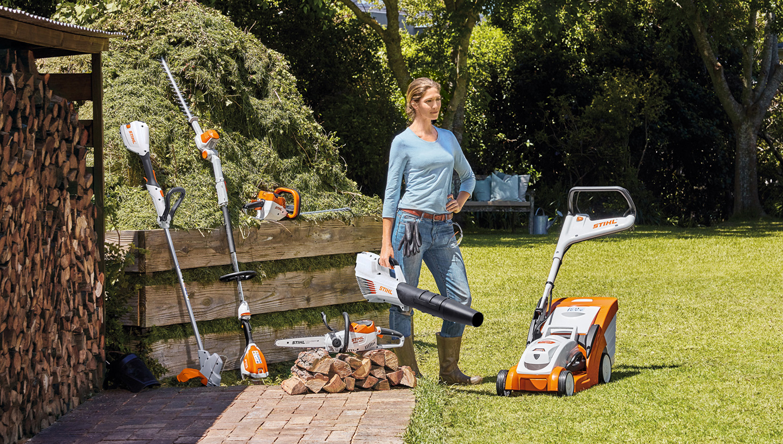 Μια γυναίκα στέκεται στον κήπο με μια ποικιλία προϊόντων επαναφορτιζόμενης μπαταρίας της STIHL