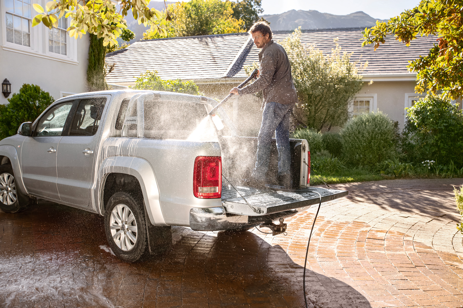 Άνδρας στέκεται στην επιφάνεια φόρτωσης ενός pickup και πλένει το αυτοκίνητο με ένα πλυστικό υψηλής πίεσης