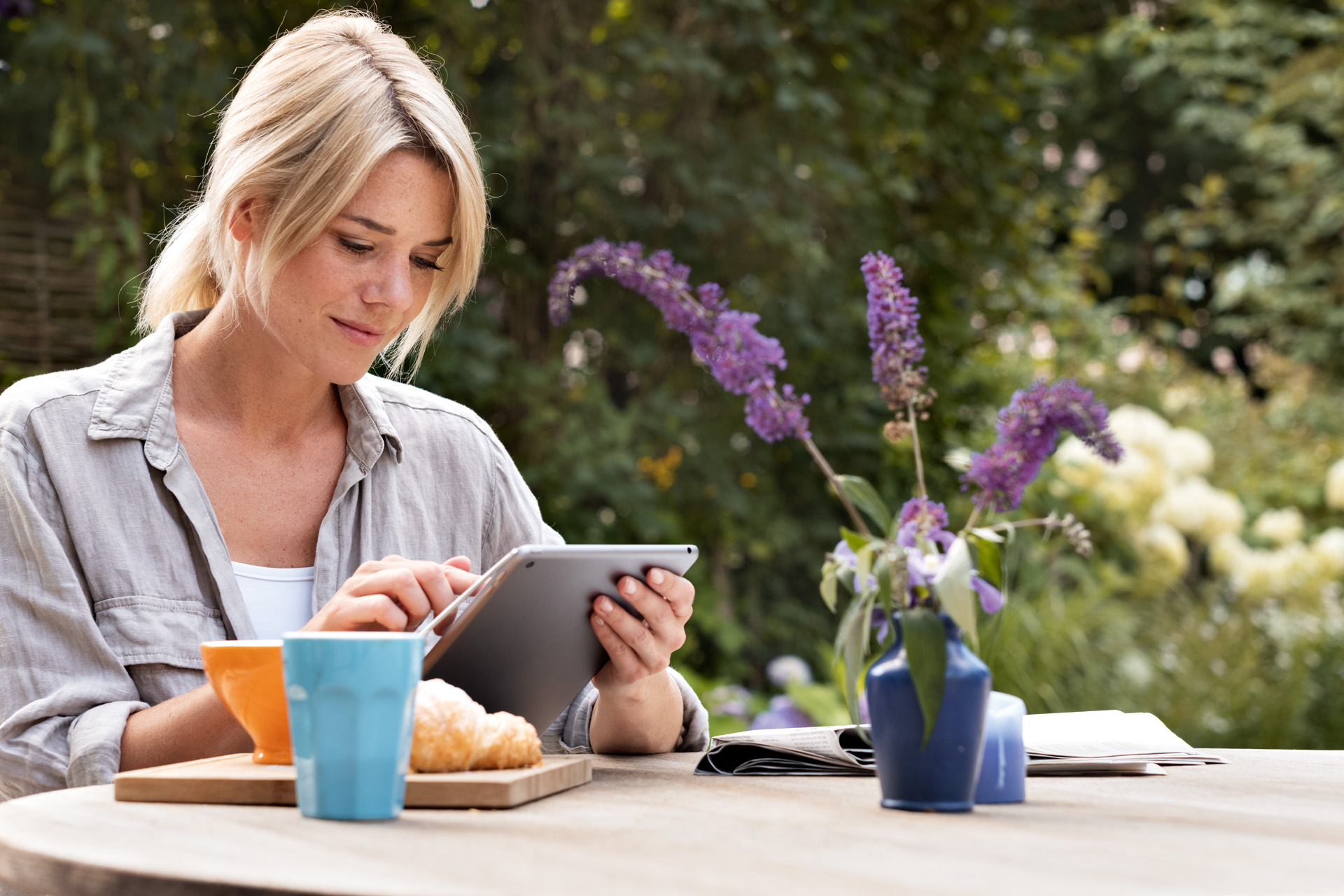 Μια γυναίκα χρησιμοποιεί ένα tablet στο τραπέζι πρωινού στον κήπο